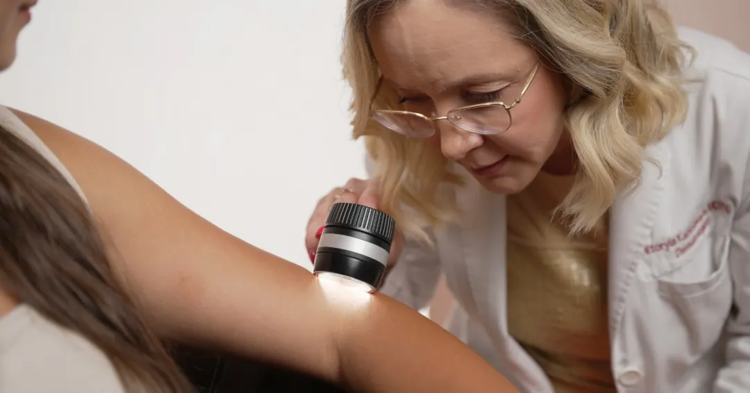 Dr. Viktoryia Kazlouskaya examining a mole with a dermatoscope during a skin cancer screening.